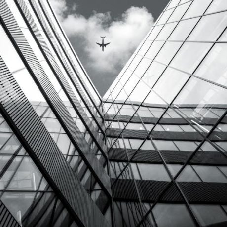 Flying airplane over modern architecture building, low angle black and white high contrast picture